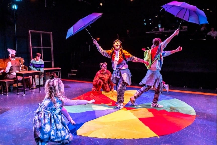 Two people holding umbrellas, and dancing upon a multi-colored circle. From the on-stage play: Alice in Wonderland by Bad Hat Theatre in Toronto, Ontario, Canada.