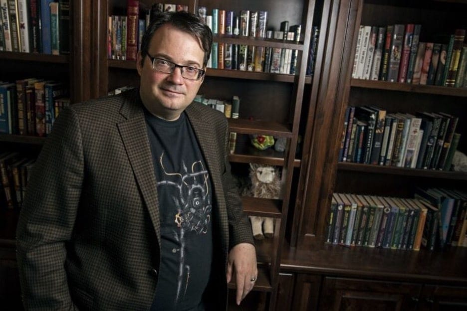 Science fiction/fantasy writer Brandon Sanderson standing in front of full bookshelves.