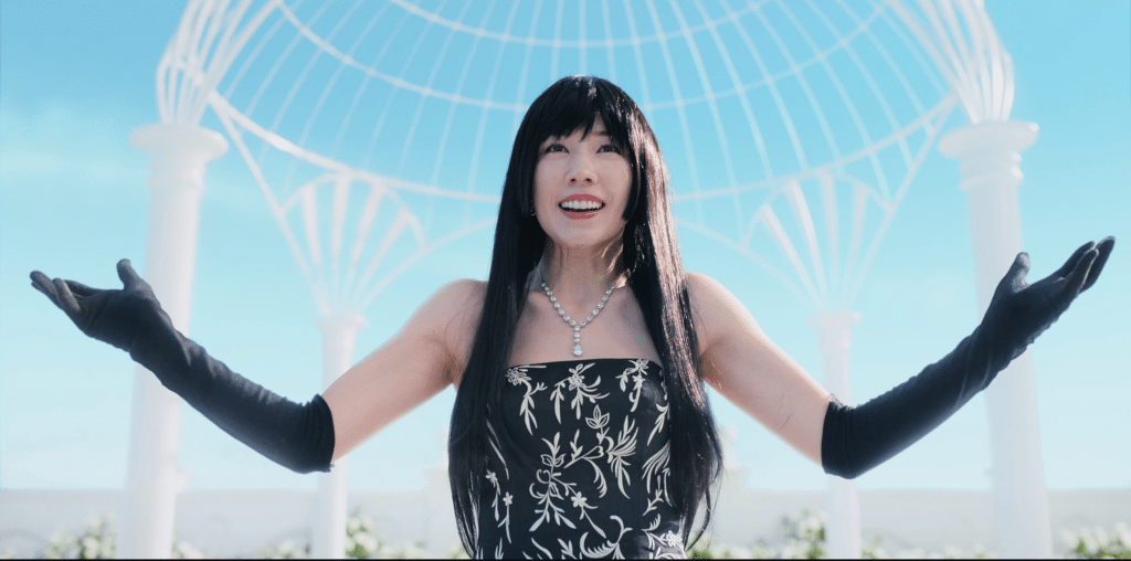 Riisa Naka, wearing a black and white dress and black gloves, smiles and raises her hands in a still from the Netflix science fiction series "Alice in Borderland."