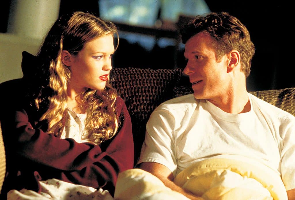 Julia Stiles and William R. Moses sitting on a couch in a production still from the 1998 thriller "Wicked".