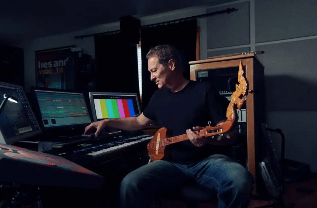 "Wicked" composer Cliff Martinez in his studio, working with a guitar, keyboard, and software interface.