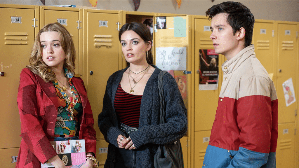 Still image of Aimee Lou Wood, Emma Mackey, and Asa Butterfield standing in front of yellow lockers from the Netflix series "Sex Education". 