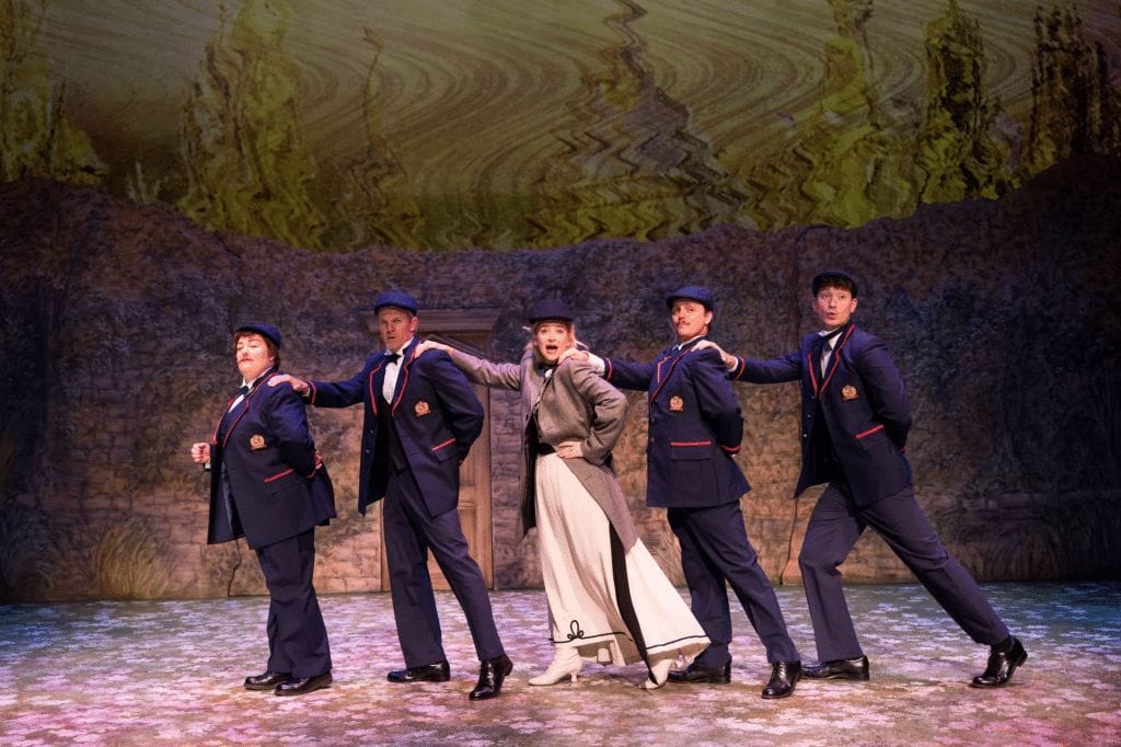 A still image featuring Alice Liddell and glee singers from the production of the musical "Alice, Formerly of Wonderland".