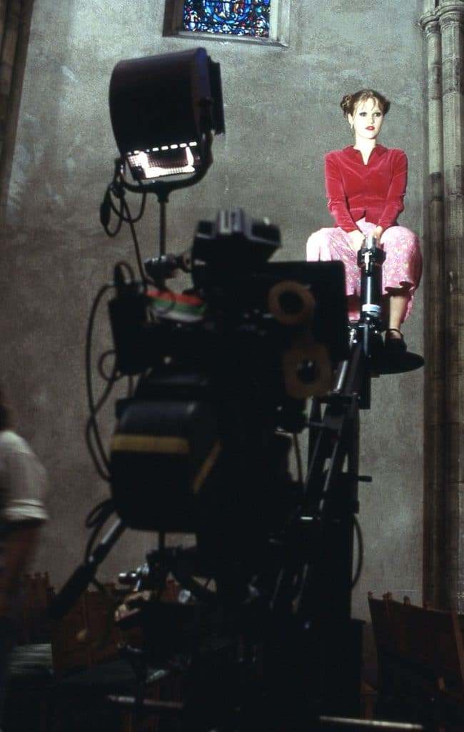 Photograph of actor Julia Stiles sitting on a crane with a film camera in the foreground from the set of the 1998 thriller "Wicked".